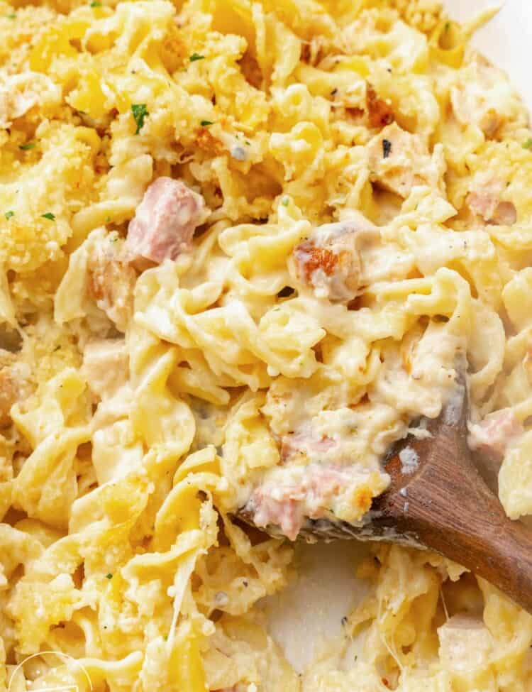 Close up shot of creamy Chicken Cordon Bleu Casserole with a wooden serving spoon