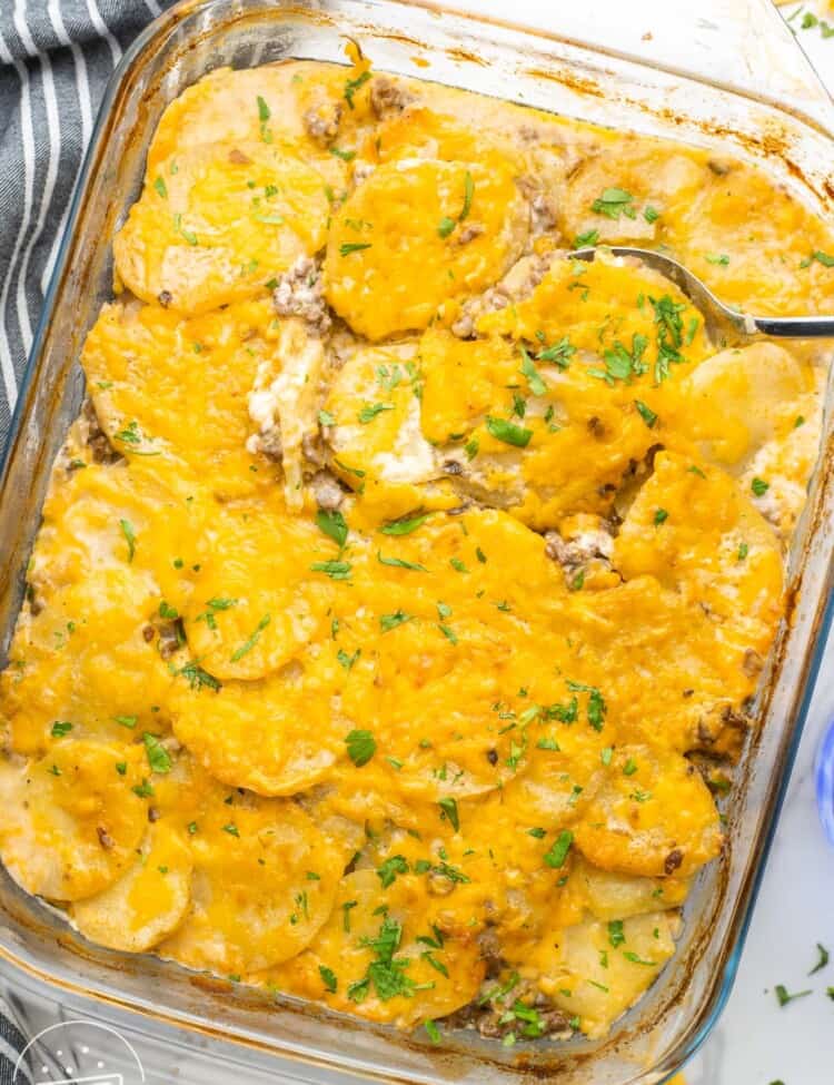 a glass 9x13 inch baking dish filled with potato and hamburger casserole, topped with melted cheese and fresh parsley.