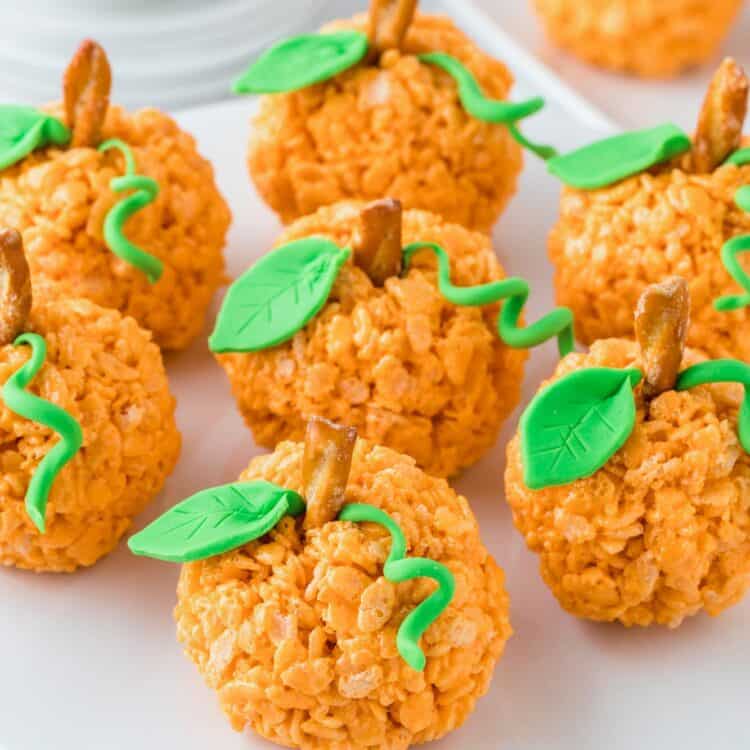 7 pumpkin rice krispie treats on a white cake pedestal.