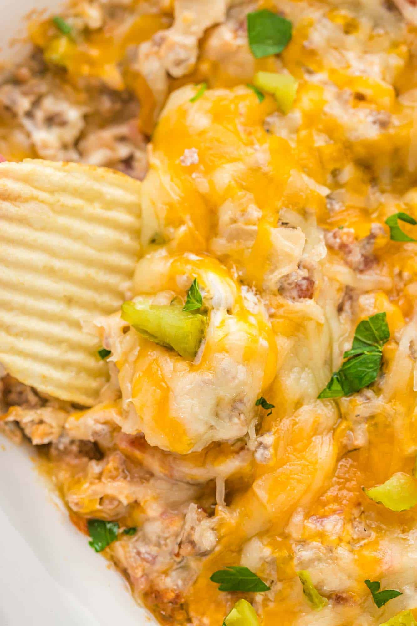 Dipping a potato chip in melty cheese and cheeseburger dip
