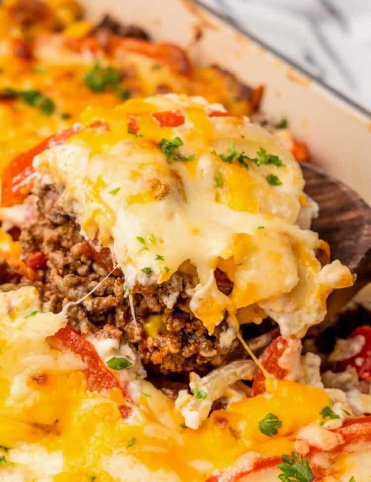 a square of layered john wayne casserole with ground beef and cheese, being lifted out of the dish with a spatula