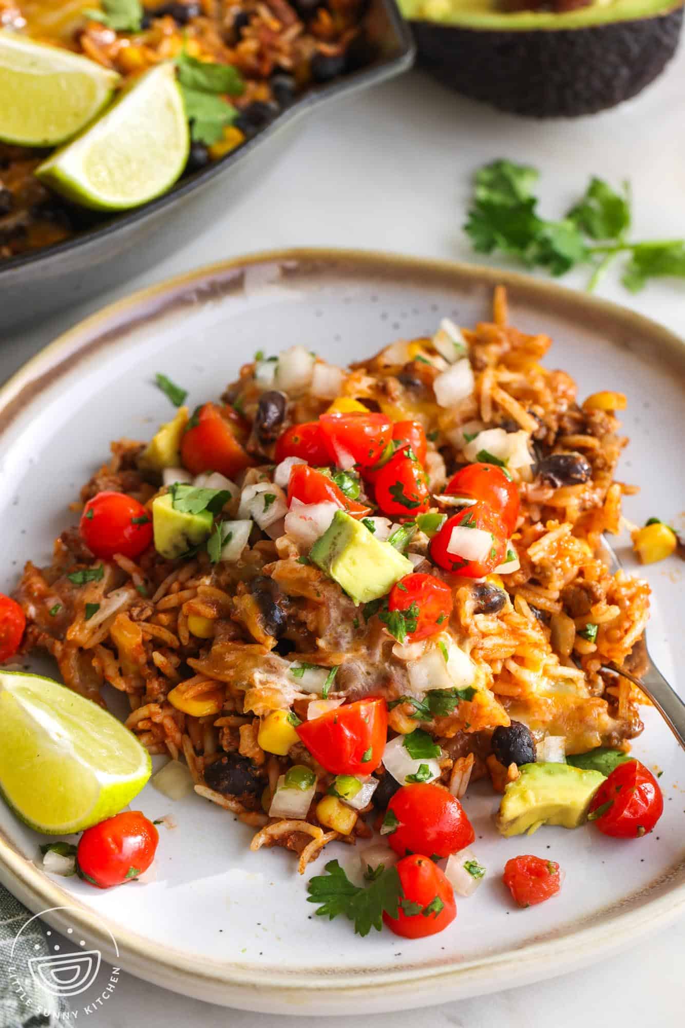 a serving of Mexican beef and rice skillet, topped with fresh tomato salsa with a lime wedge on the side.