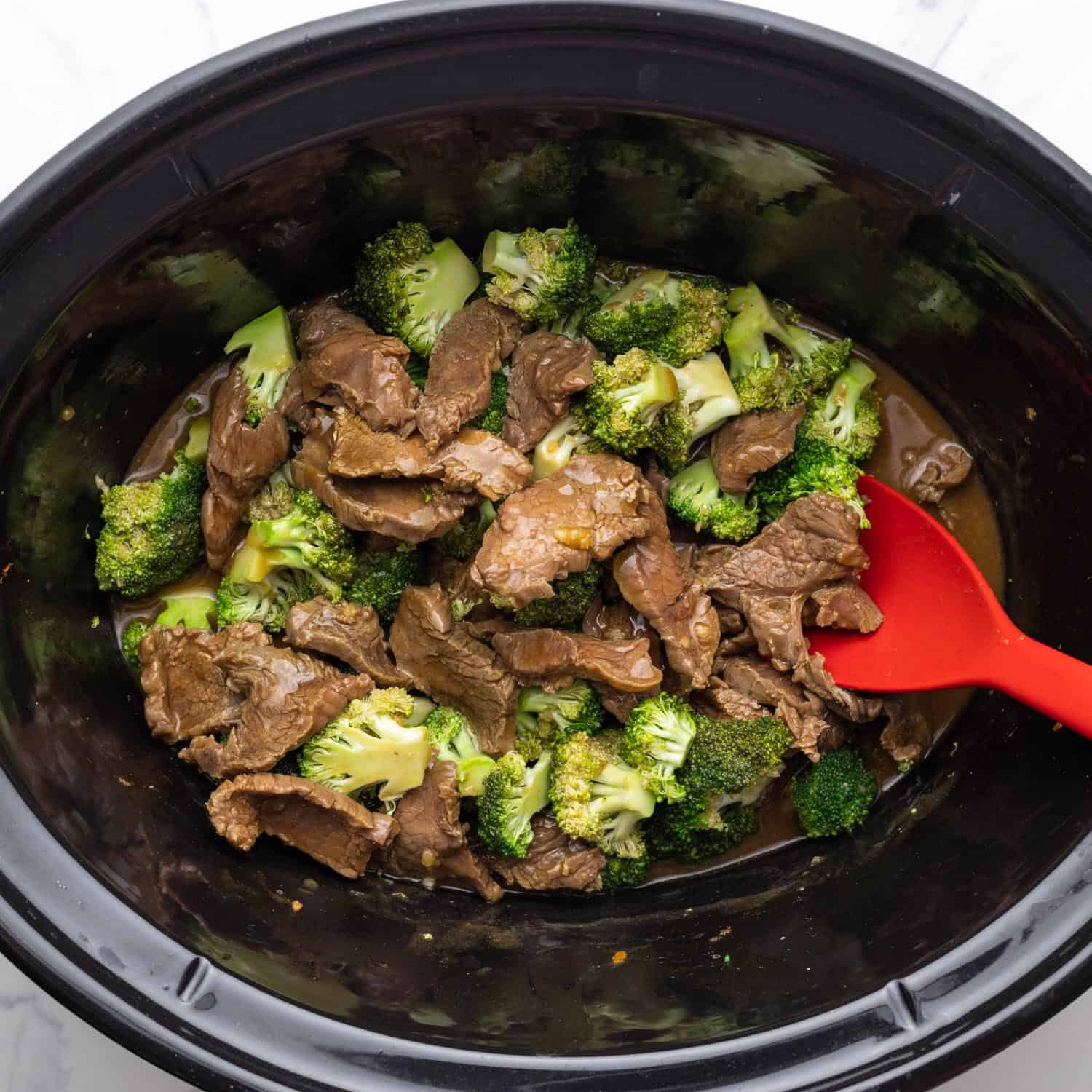 slow cooker beef and broccoli, stirred with a red spoon.