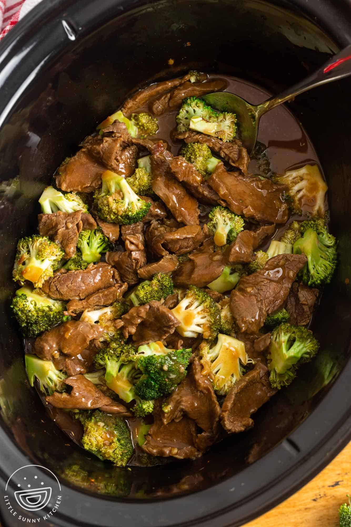 saucy chinese slow cooker beef and broccoli in the pot, stirred with a metal spoon.