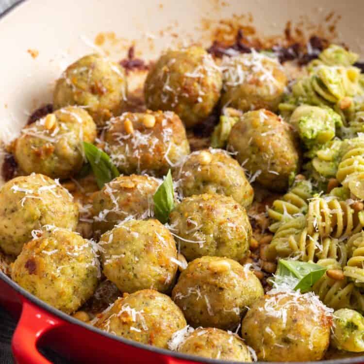 a skillet of chicken meatballs with pesto rotini pasta with pine nuts.
