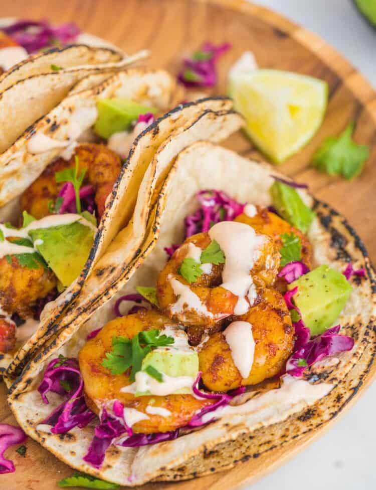 Grilled shrimp tacos with avocado, creamy sauce, and fresh cilantro. Placed on a wooden tray.