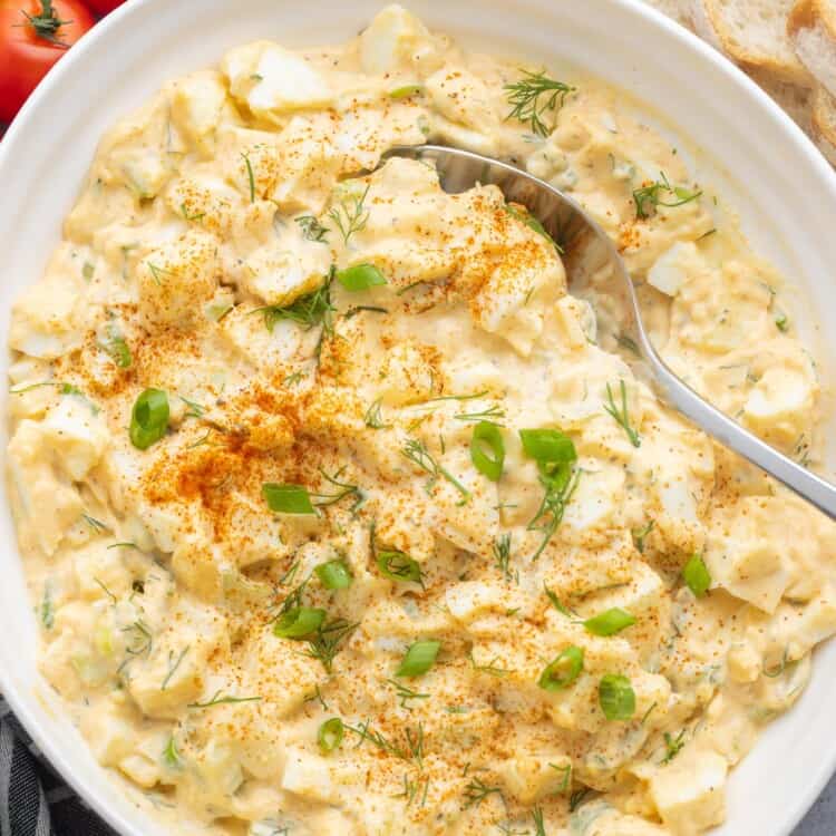 A large serving bowl of egg salad with large pieces of eggs, garnished with dill and green onion.