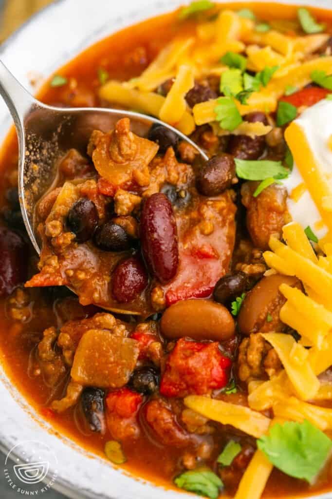 a large soup spoon in a bowl of chili with cheese and beans.