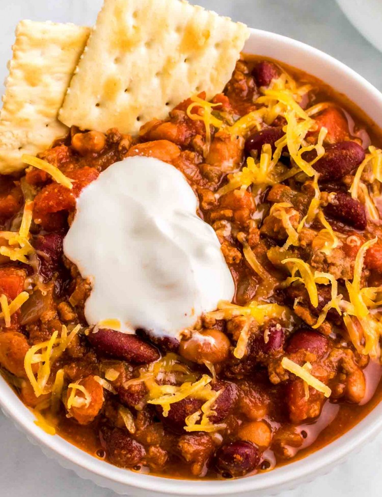 Wendy's Chili served in a white bowl with saltines, sour cream and shredded cheese.