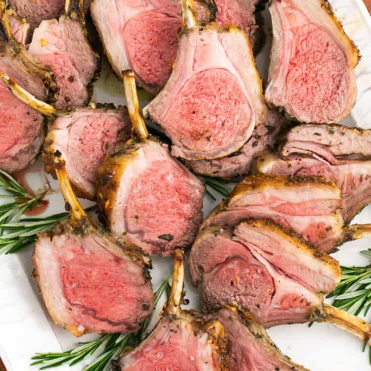 Sliced rack of lamb served on a platter, with fresh rosemary leaves.