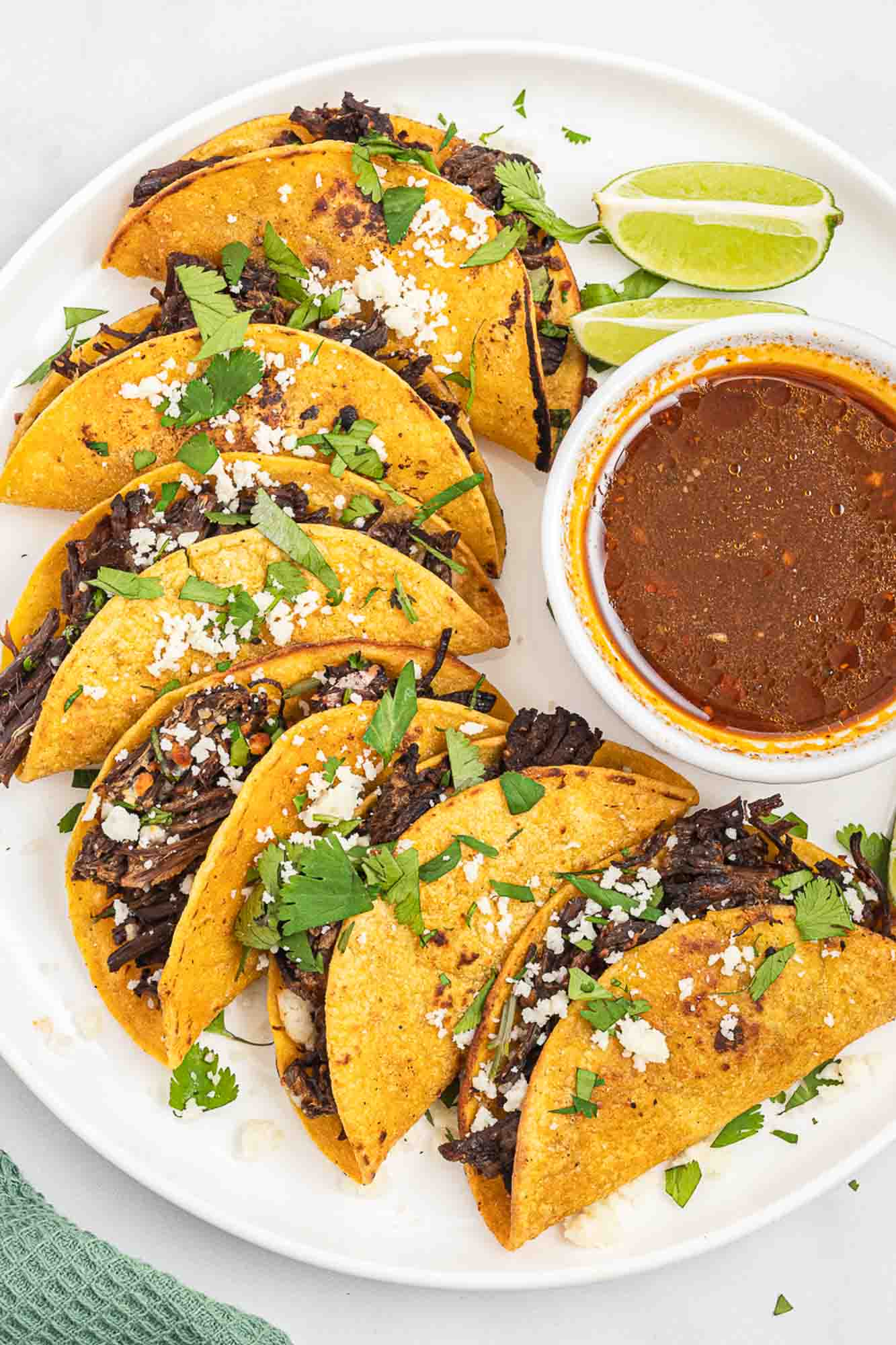 Overhead shot of birria tacos round platter, with dip in the center.