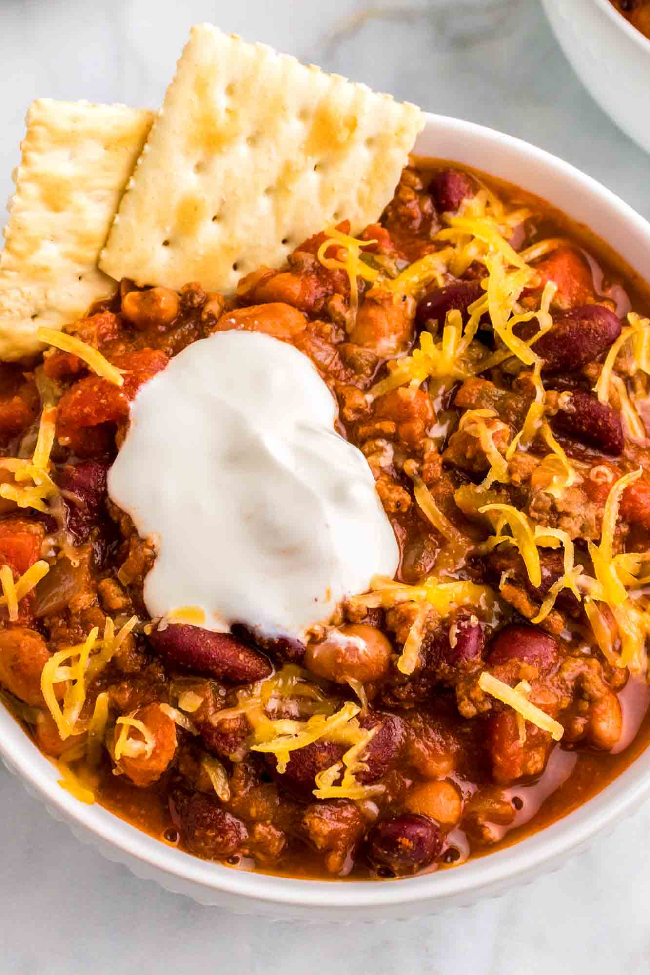 Wendy's Chili served in a white bowl with saltines, sour cream and shredded cheese.