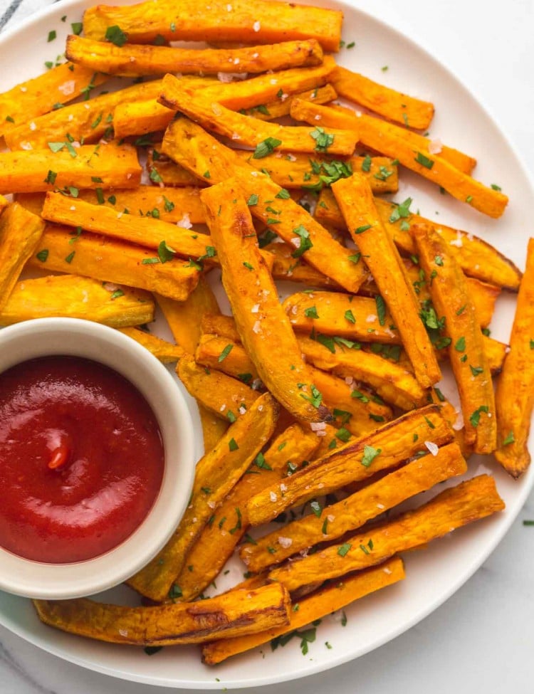 Sweet potato fries on a white plate with tomato sauce on the side