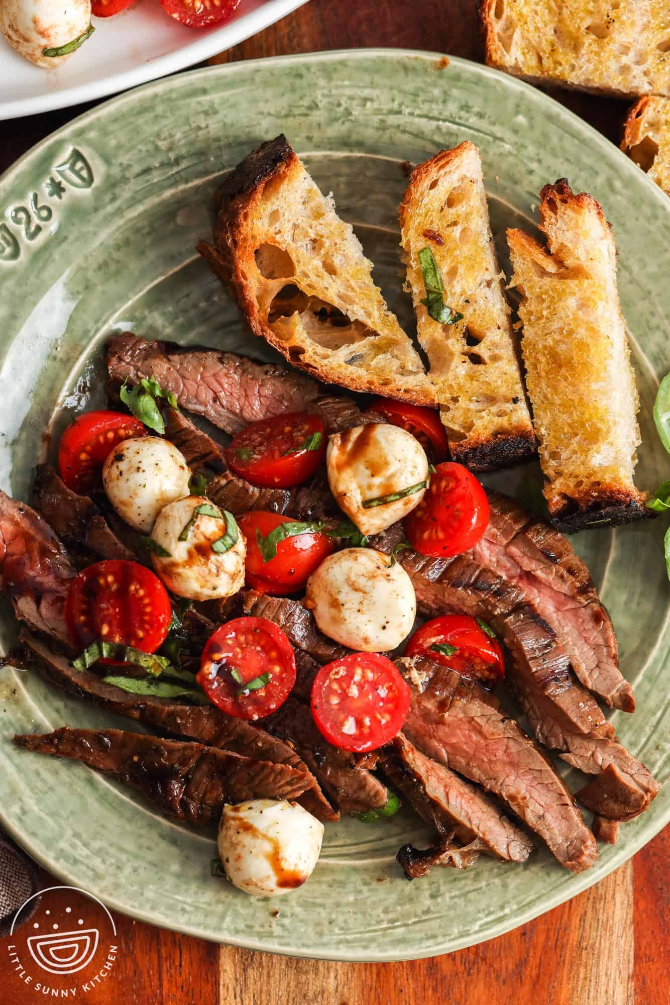 a serving of caprese steak on a ceramic plate with a side of garlic bread.