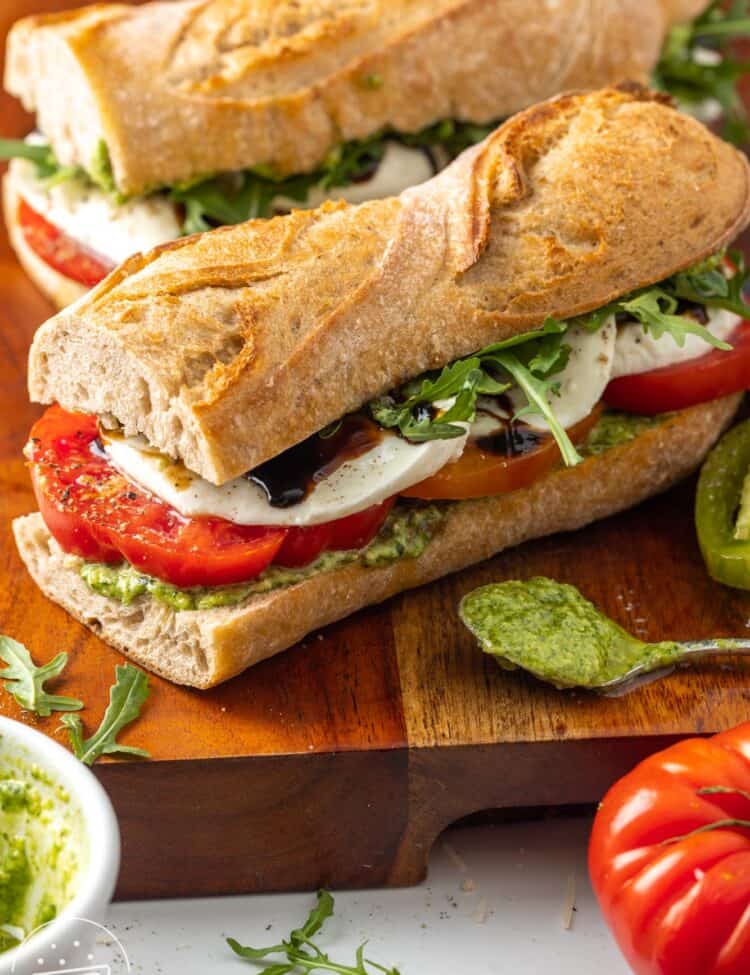 two homemade caprese sandwiches with sliced tomatoes, arugula, balsamic glaze, and sliced cheese.