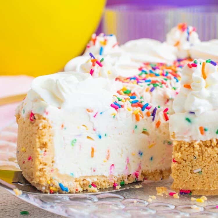 a slice of funfetti cheesecake being removed from the whole pie. In the background is a yellow and a purple balloon.