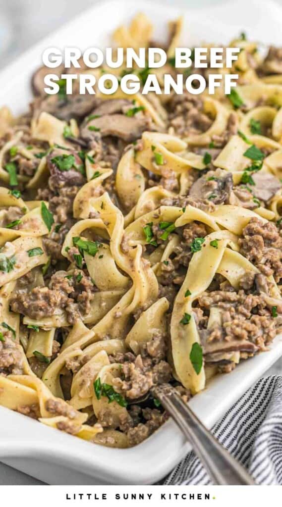 Ground beef stroganoff served in a white casserole dish, garnished with fresh parsley leaves, and overlay text that reads "ground beef stroganoff"